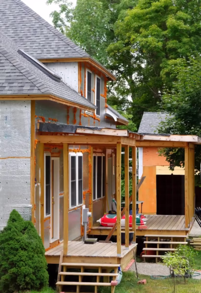 Home exterior showing ongoing renovation with new siding installation, wooden porch, and partially finished structure, relevant to windows, doors, and siding services.